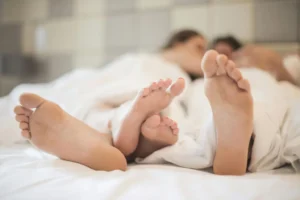 Free couple’s feet visible under blanket in a cozy bedroom, illustrating what is shallowing outercourse explained for women.