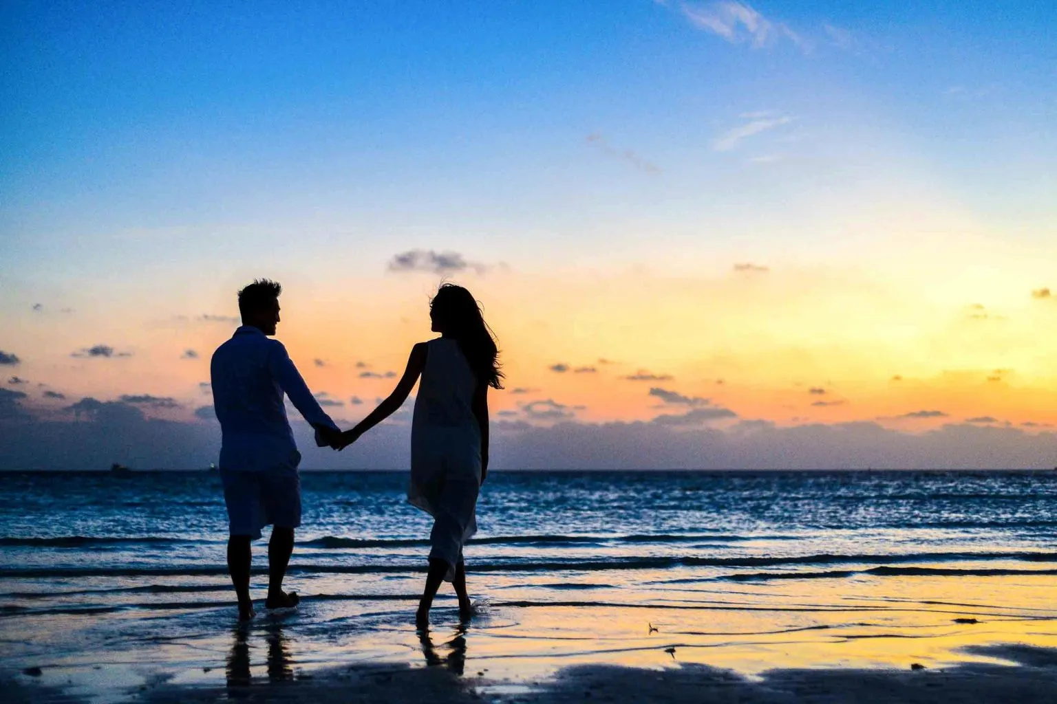 A couple holding hands and walking on the beach at sunset, symbolizing how to build trust after intimacy has faded.