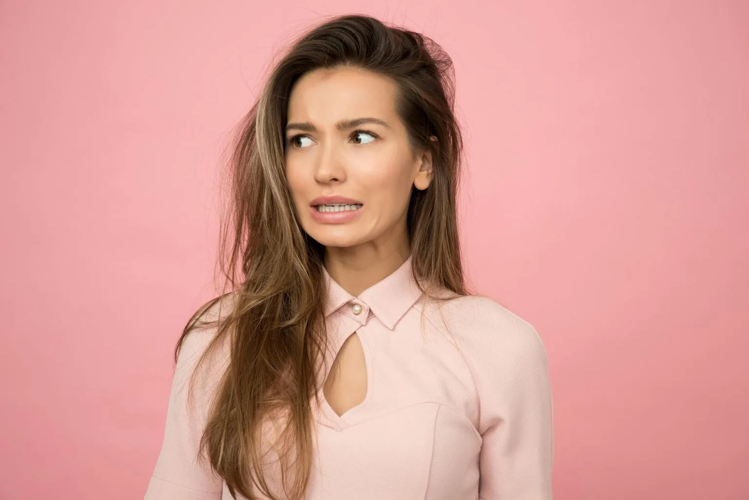 A young woman with a playful, uncertain expression illustrating the role of pheromones in female arousal myths vs facts against a pink background.