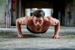 Fit shirtless man with a beard doing a push-up exercise on a concrete floor, symbolizing strength and benefits of pelvic floor exercises for men.