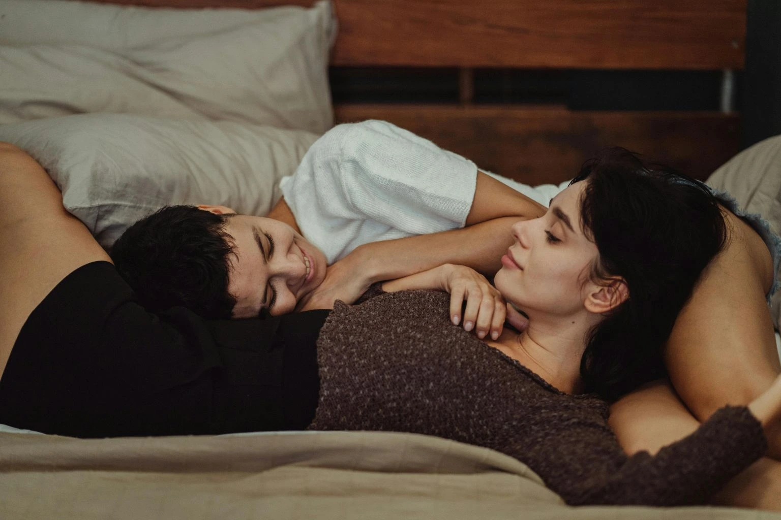 Image of a happy couple in bed, holding blocks that say "trust" and "consent," with other blocks nearby that say "honesty" and "play." This visually represents how to create a sex positive relationship through communication and respect.