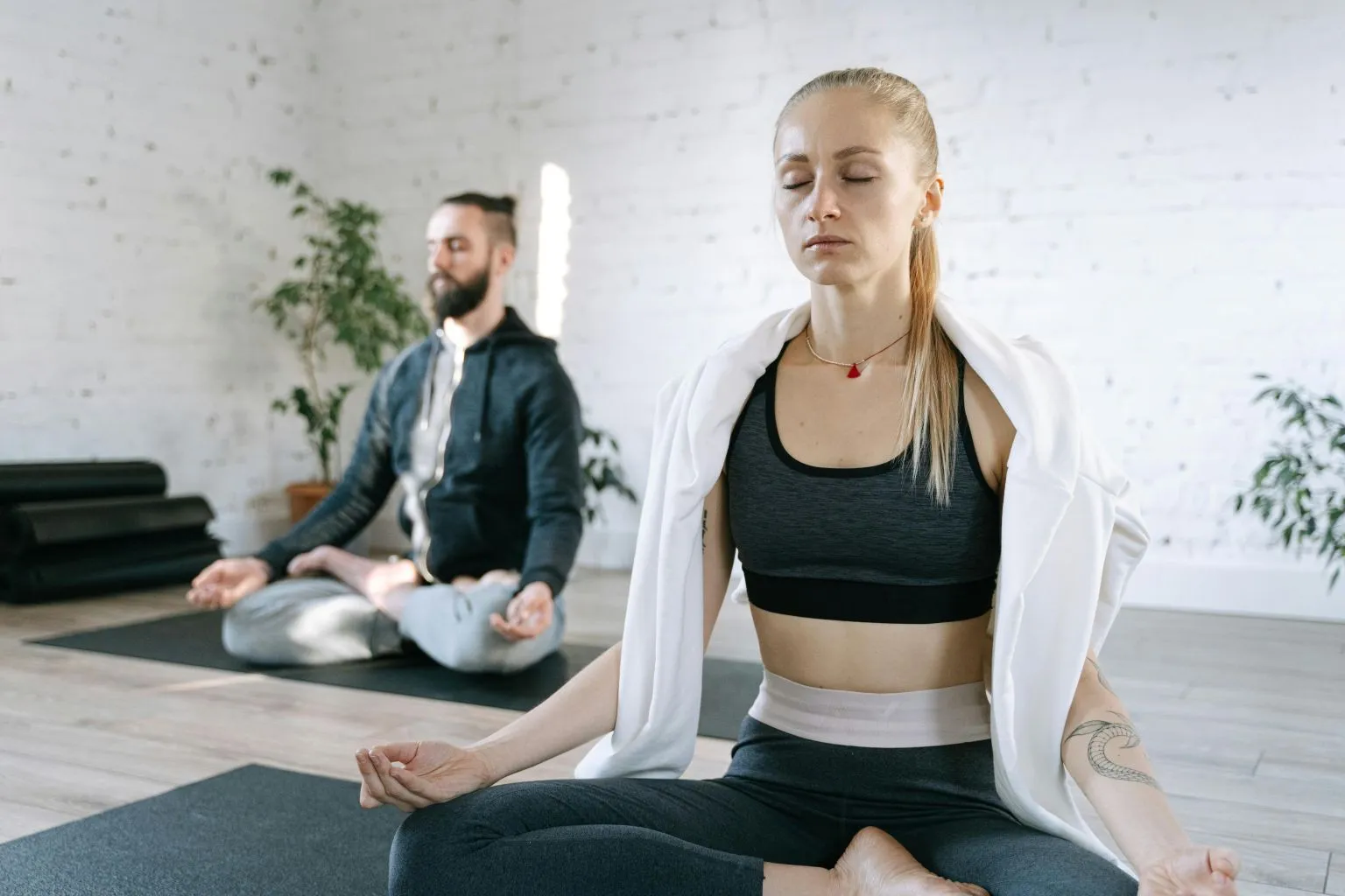 Two people meditating on yoga mats practicing the best breathing techniques for sexual relaxation in a calm, bright studio.
