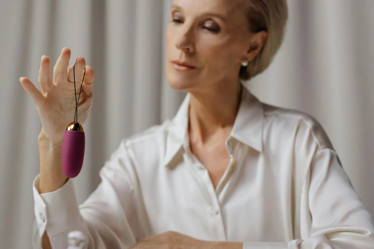 A woman holding a vibrator and thoughtfully smiling, reflecting on the question — do women enjoy solo play and the empowerment it brings.